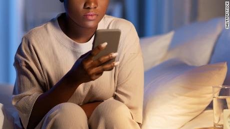 technology, internet, communication and people concept - young african american woman with smartphone lying in bed at home at night