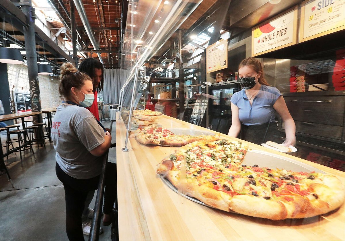 <i>John Hart/Wisconsin State Journal</i><br/>Ian's Pizza worker Stella Klein serves customers Olivia Rebholz and Randy Bland at the restaurant's Garver Feed Mill location. Only three of the chain's seven restaurants were approved for federal COVID-19 grant assistance.