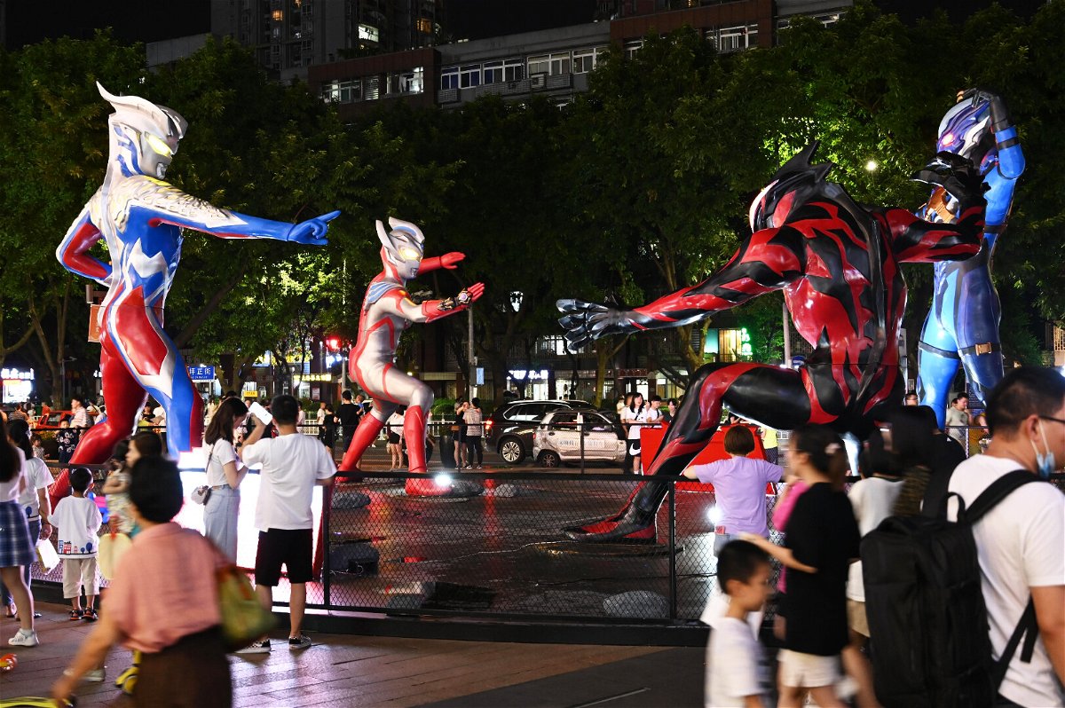 <i>Chen Chao/China News Service/Getty Images</i><br/>People watch sculptures of Ultraman and a monster outside a shopping center on July 17 in Chongqing