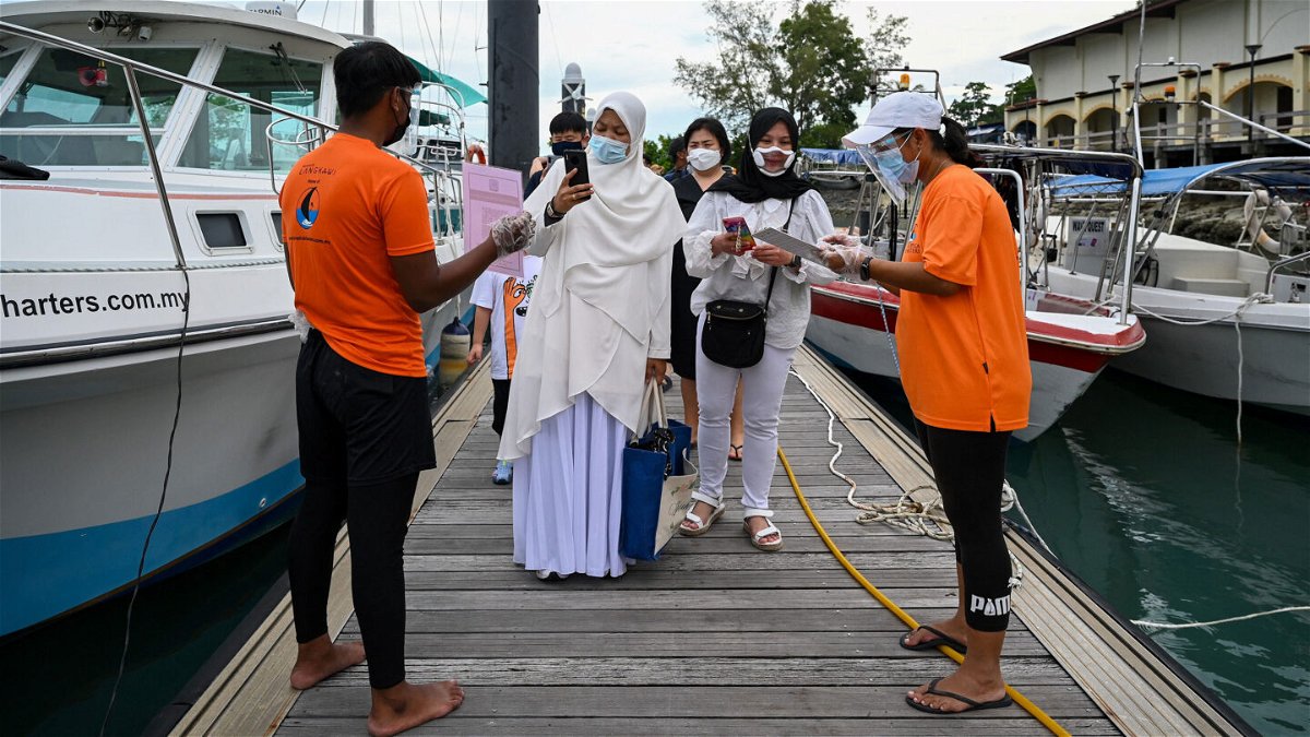 <i>MOHD RASFAN/AFP via Getty Images</i><br/>Passengers scan an app to monitor their health status before boarding a yacht in Langkawi