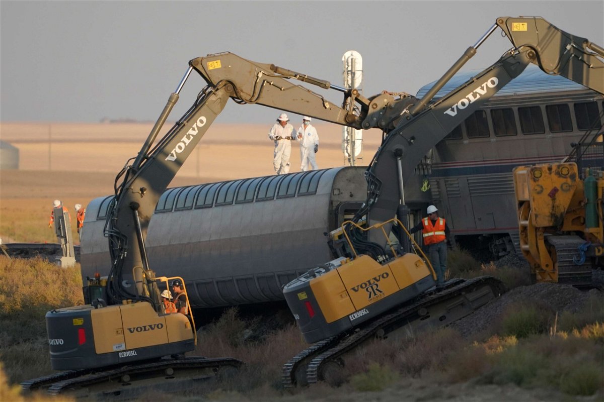 <i>Ted S. Warren/AP</i><br/>Workers stand on a train car on its side as front-loaders prop up another train car