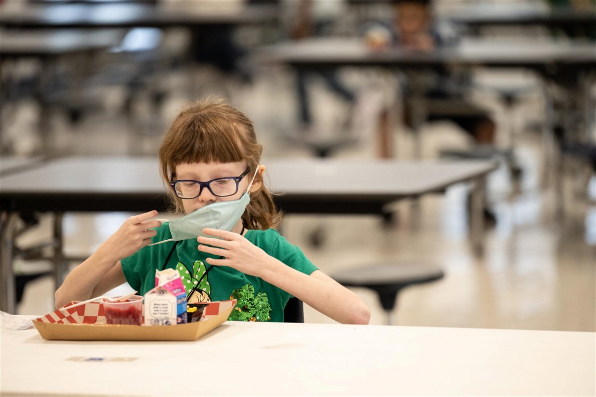<i>Jon Cherry/Getty Images</i><br/>A child puts her mask back on after finishing lunch at a socially distanced table in the cafeteria of Medora Elementary School on March 17