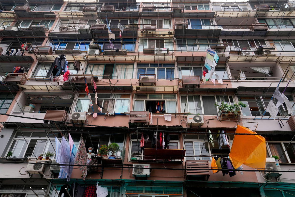 <i>Ng Han Guan/AP</i><br/>A resident wearing a mask looks out from his home in Shanghai on Thursday.