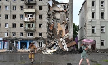 A local resident walks past a Ukrainian rescuer working outside a building partially destroyed after a Russian missile strike in Kharkiv on July 11 amid Russia's military invasion launched on Ukraine.
