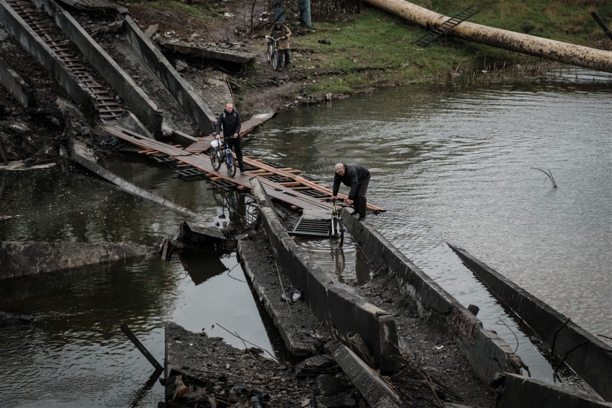 <i>Yasuyoshi Chiba/AFP/Getty Images</i><br/>Men cross the destroyed bridge with their bicycles in the frontline town of Bakhmut in the Donetsk region on October 11.