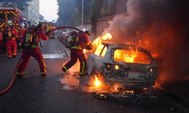 Firefighters work to put out a burning car at a protest in Nanterre