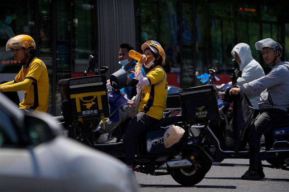 <i>Andy Wong/AP</i><br/>A delivery rider drinks water as she and other motorists wait to cross a street on a hot day in Beijing