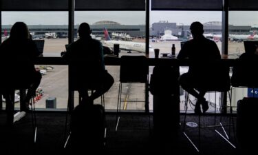 Passengers are seen in silhouette at a Delta Sky Club as an airplane parks at a gate in front of them at Hartsfield-Jackson Atlanta International Airport ahead of the Fourth of July holiday in Atlanta