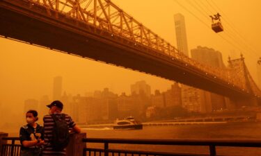 People wear protective masks as the Roosevelt Island Tram crosses the East River while haze and smoke from the Canadian wildfires shroud the Manhattan skyline.