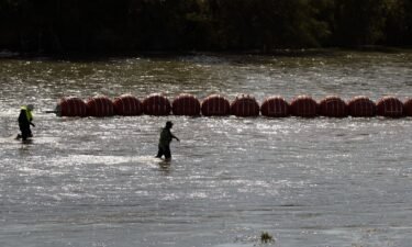 Workers help deploy a string of large buoys to be used as a border barrier at the center of the Rio Grande near Eagle Pass