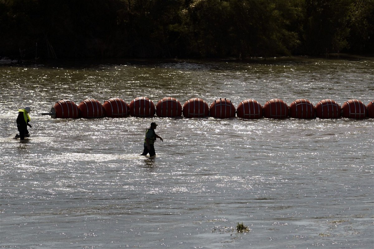 <i>Eric Gay/AP</i><br/>Workers help deploy a string of large buoys to be used as a border barrier at the center of the Rio Grande near Eagle Pass