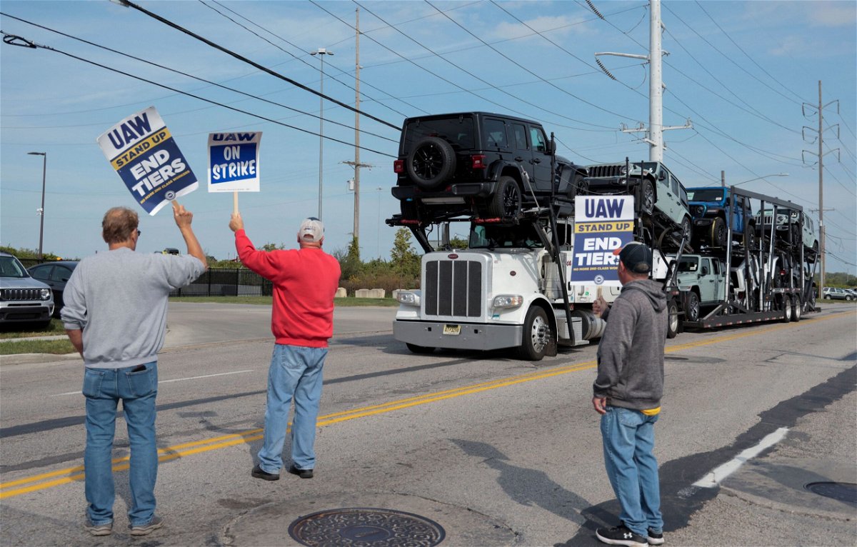 <i>Rebecca Cook/Reuters</i><br/>A car hauler transporting Jeep Wranglers drives past striking United Auto Workers members outside the Stellantis Jeep Plant in Toledo