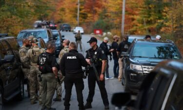 Law enforcement officials gather in the road leading to the home of the suspect being sought in connection with two mass shootings on October 26