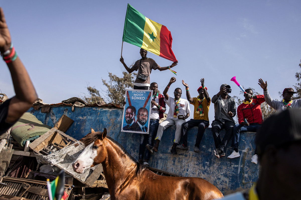 <i>John Wessels/AFP/Getty Images via CNN Newsource</i><br/>A supporter of the coalition of anti-establishment candidates holds a Senegalese flag as they sit on top of a wall during a campaign rally in Dakar on March 10.