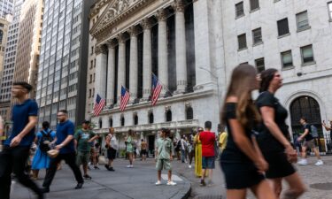 People walk through the financial district by the New York Stock Exchange (NYSE) on August 14