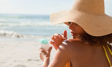 Young beautiful woman applying sunscreen on her shoulder while sitting on the beach.