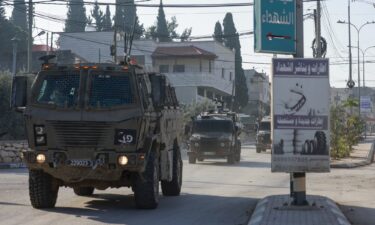 Israeli army vehicles drive down a road during a raid in Qabatiya