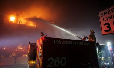 A Los Angeles Fire Department firefighter sprays water on a burning apartment complex caused by the rapidly spreading Palisades Fire in Los Angeles.