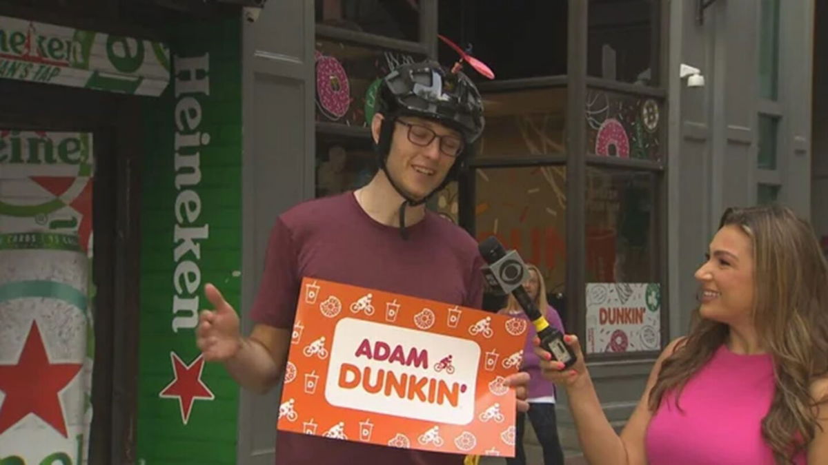 <i>WBZ via CNN Newsource</i><br/>Adam Bigelow holds one of the signs that Dunkin' made in support of his ride.