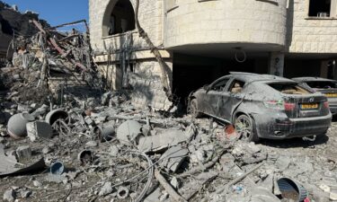Men walk near a damaged vehicle at an impact site following missile attack from Iran in Tamra