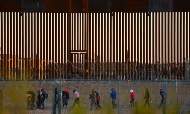 Migrants seeking asylum in the United States gather near the border wall after crossing a razor wire fence as a member of the Texas National Guard escorts them in December 2024.