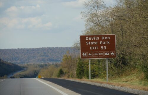 A roadside sign with exit directions to Devils Den State Park at Interstate 49