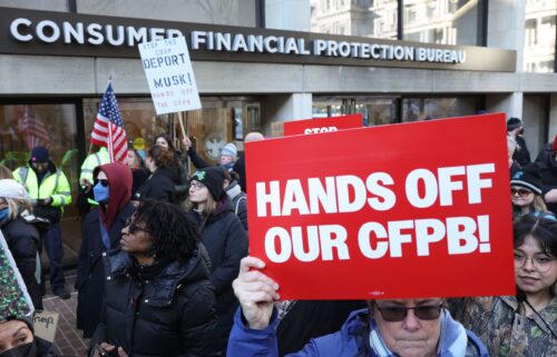 Demonstrators raise signs and posters during a rally outside the Consumer Financial Protection Bureau headquarters in Washington