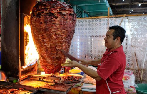 A server cuts from a large spit of meat that's roasting in a food stand in the municipal market in Mérida