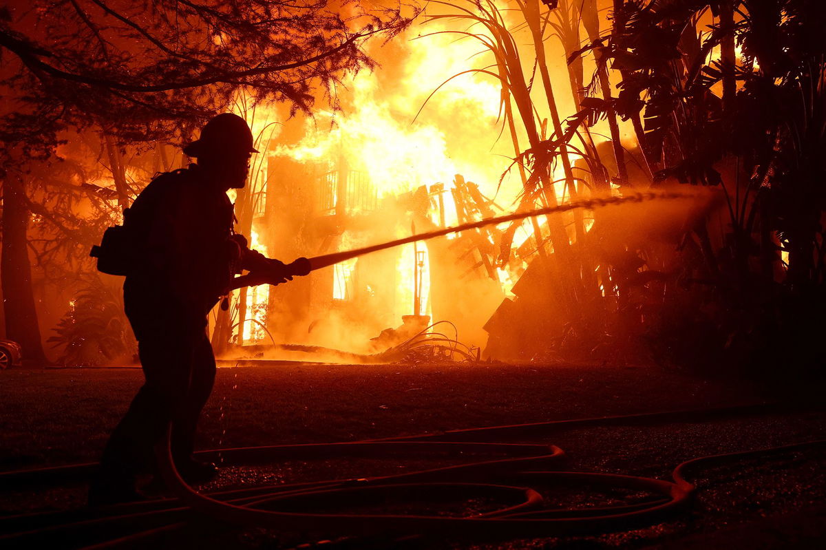 <i>Justin Sullivan/Getty Images via CNN Newsource</i><br/>Los Angeles County firefighters spray water on a burning home as the Eaton Fire moved through the area on January 8 in Altadena